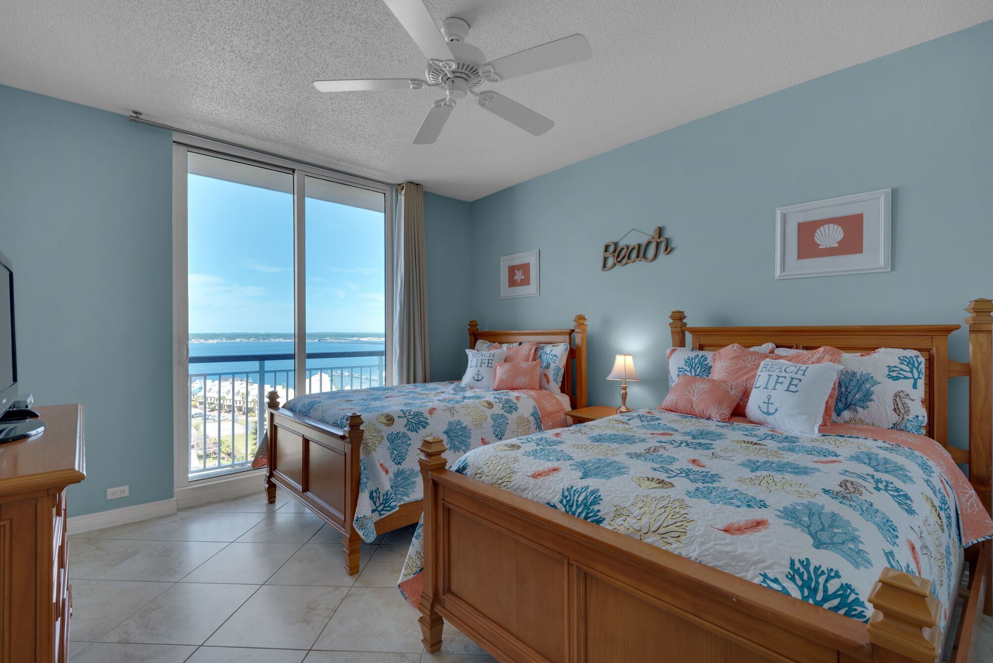 A bedroom with two beds, a ceiling fan, and a view of the beach.