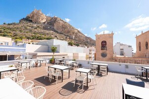 A rooftop terrace with outdoor seating, a clock tower, and a mountain in the background.