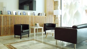 Eine moderne Hotelhalle mit Flachbildfernseher, Holzvertäfelung, schwarzen Ledersofas, einem kleinen Couchtisch und einem gemusterten Teppich.