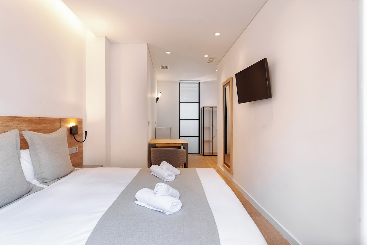 Een moderne hotelkamer met een groot bed, een houten hoofdbord, een flatscreen televisie aan de muur en een klein tafeltje met een stoel.