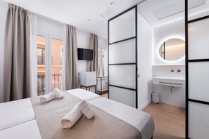 Une chambre d’hôtel comprenant un lit, une télévision, une salle de bain avec un lavabo et un miroir, et un balcon avec des rideaux.
