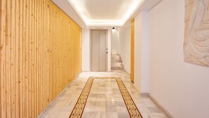 Ein moderner Korridor mit Holzverkleidung an einer Seite, einem Marmorboden mit geometrischem Muster und einer Treppe, die zu einer anderen Ebene führt.