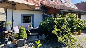 Una casa con techo de tejas, un patio con mobiliario exterior y plantas en macetas.