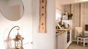 Una cocina con armarios blancos, un detalle de pared de madera, un farol colgante y una silla blanca.