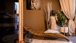 Una habitación con una silla de lounge de madera, una estatua de Buda, una planta de cactus y una alfombra estampada.