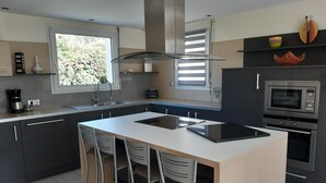 A modern kitchen with a central island, stainless steel appliances, and a window providing natural light. - single-storey house 600 m beach (Étables-sur-Mer)