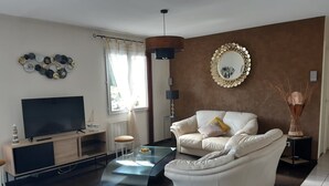 A modern living room with a flat-screen TV, a white sofa, a glass coffee table, and a decorative mirror on the wall. - single-storey house 600 m beach (Étables-sur-Mer)