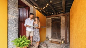 Un couple se tient sur un escalier en pierre, à l’extérieur d’un bâtiment dont le mur est jaune et qui présente des poutres en bois.