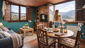 Une cuisine chaleureuse avec des meubles en bois, une table à manger dressée pour deux personnes et une vue sur les montagnes par de grandes fenêtres.