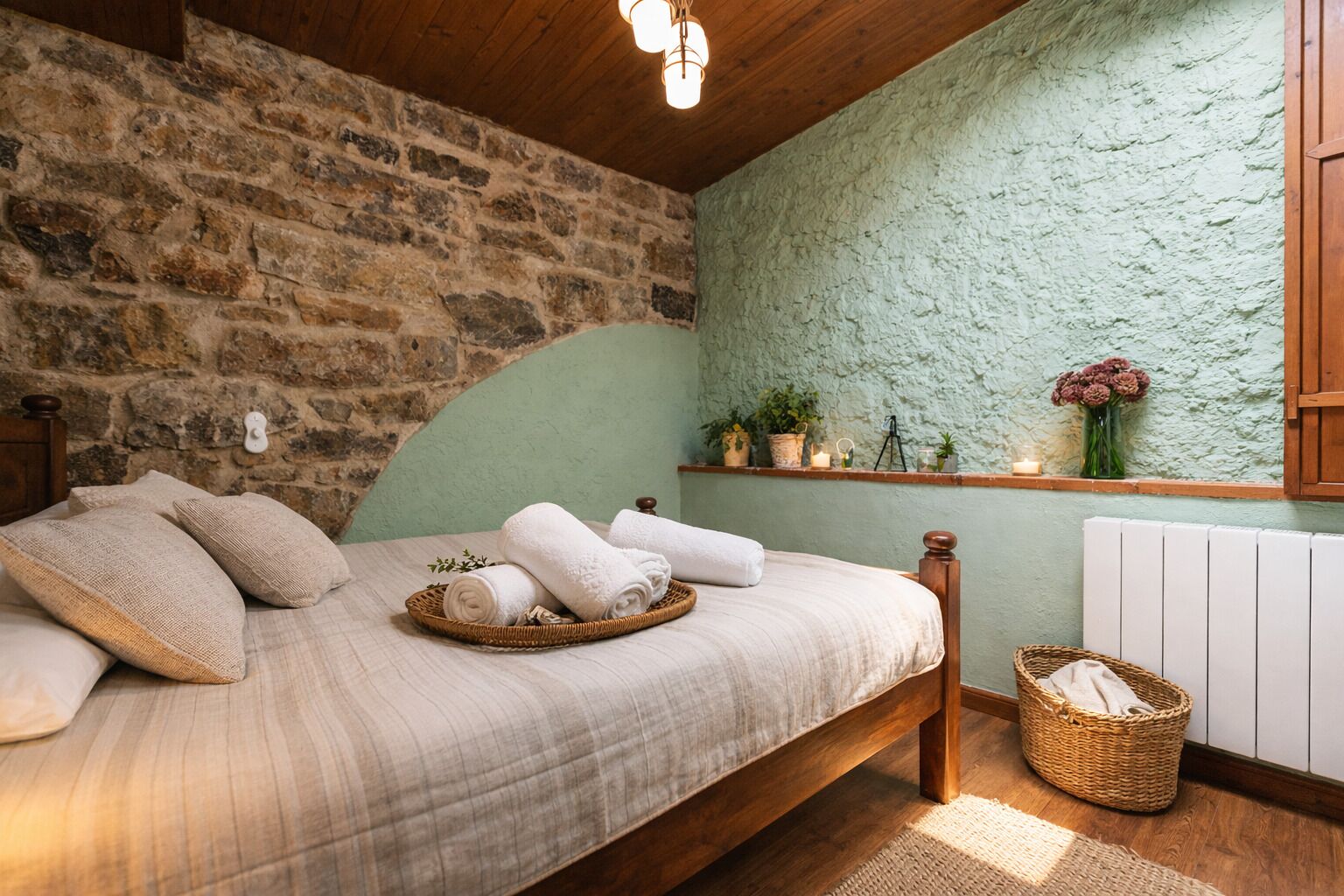 Een knus slaapkamer met een stenen muur, een houten plafond en een bed met opgerolde handdoeken.