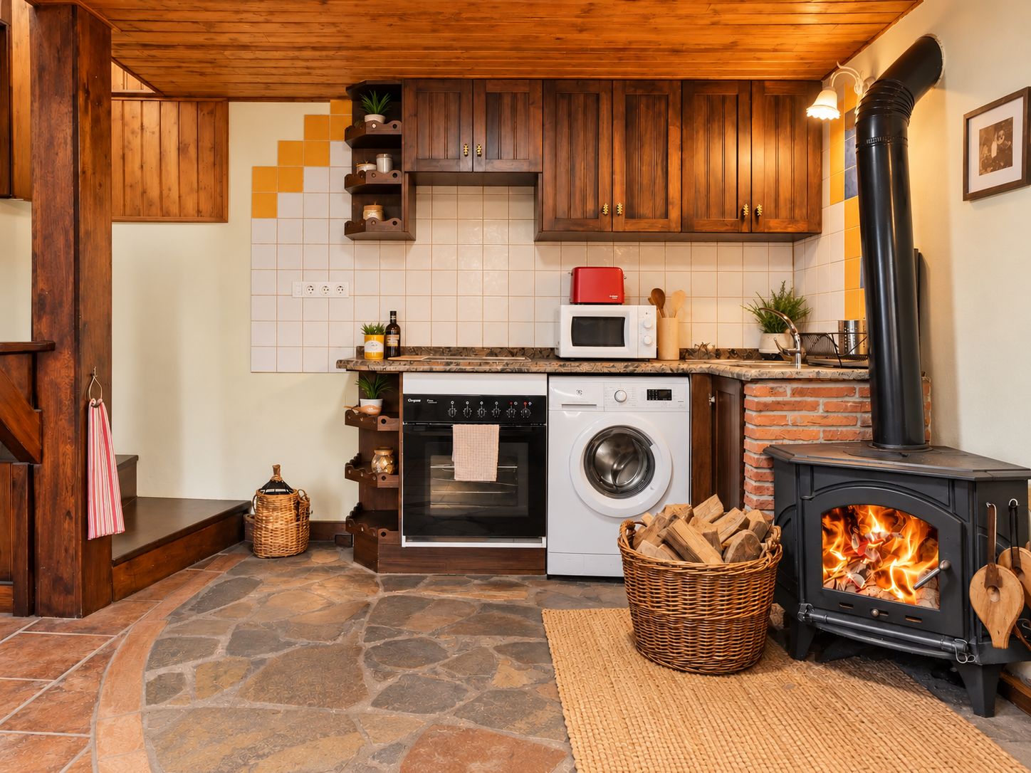 A kitchen with wooden cabinets, a stone floor, a wood-burning stove, a washing machine, and a microwave.