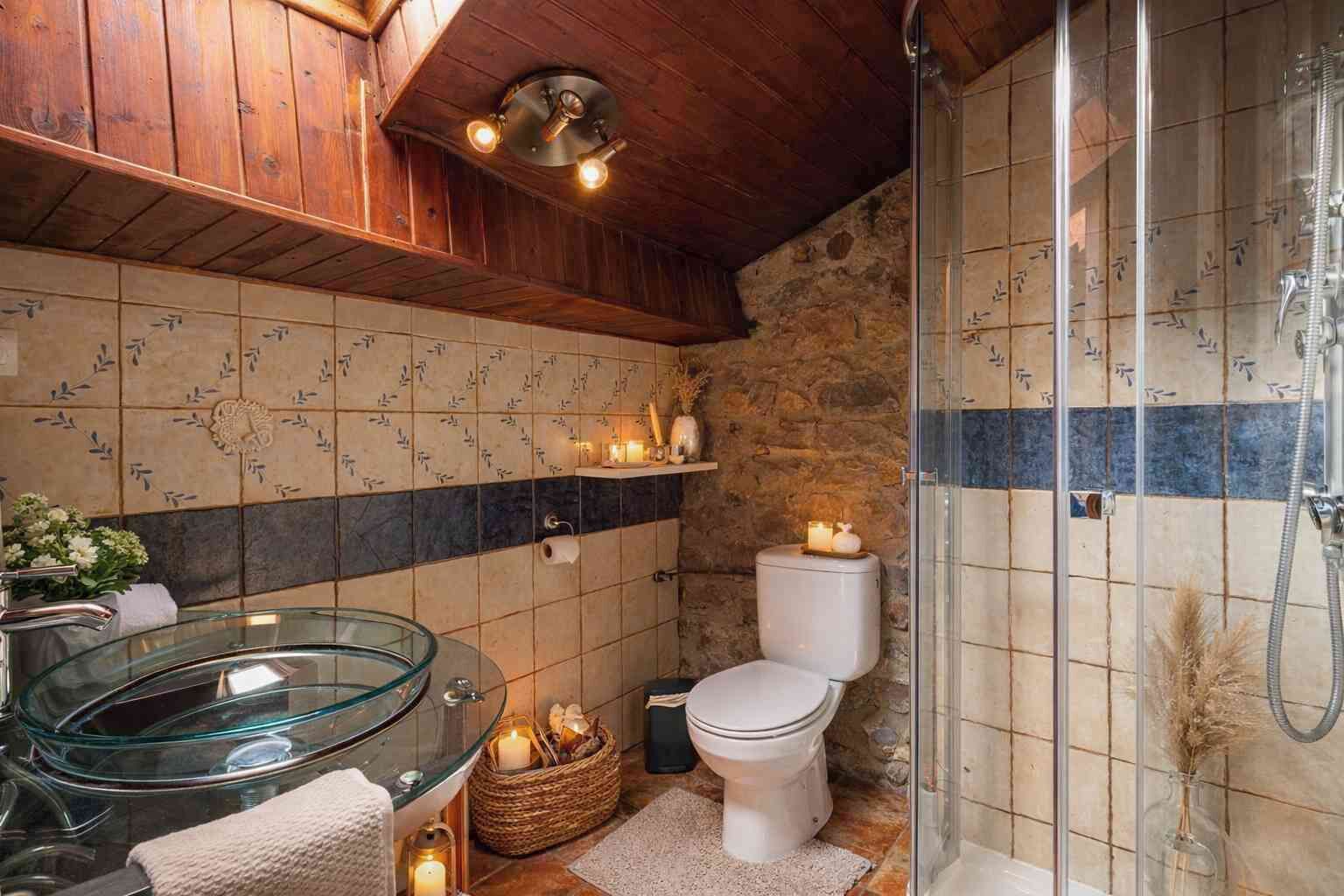 Une salle de bain avec une baignoire en verre, des toilettes, une douche et un mur en pierre.