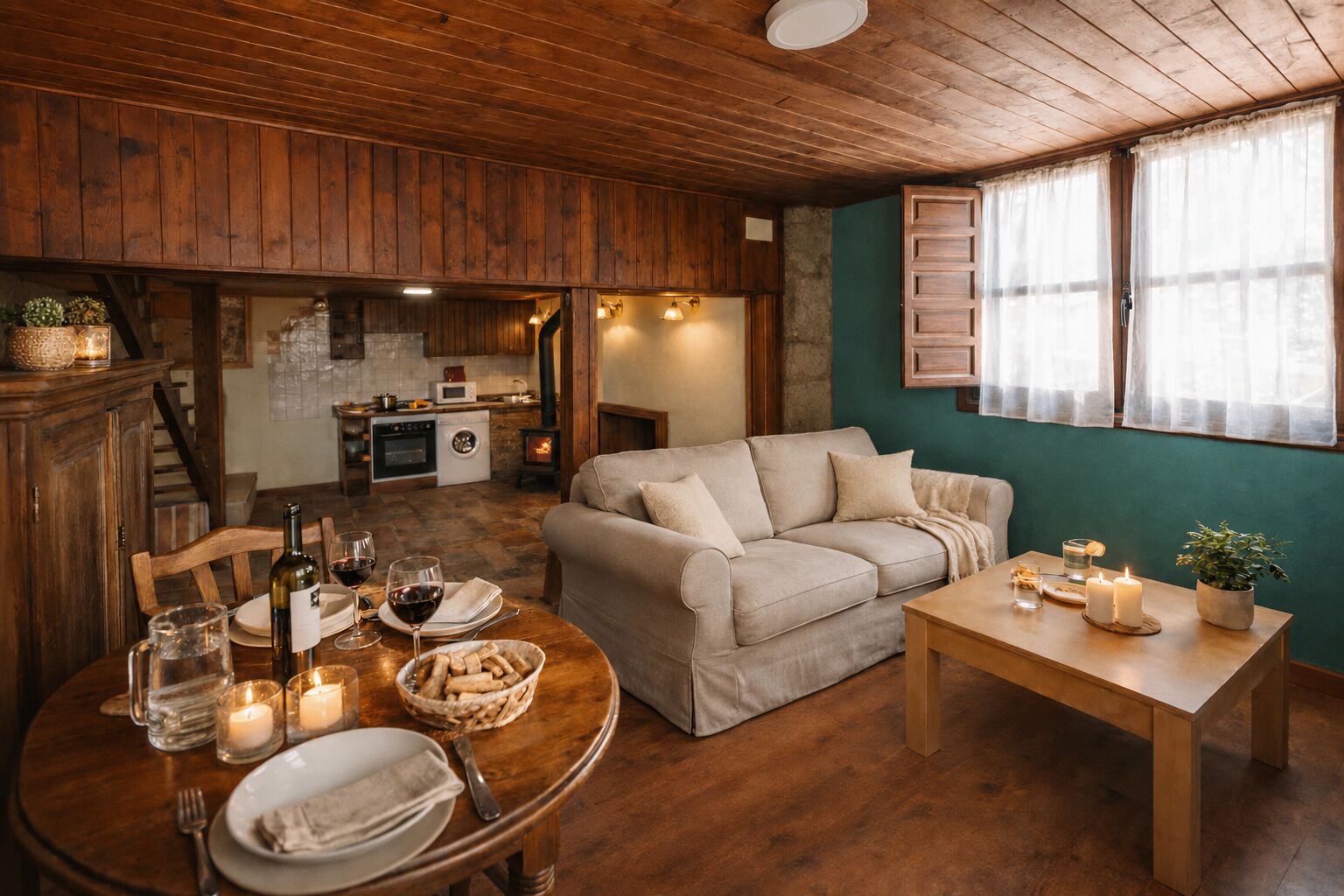 Een gezellige kamer met houten plafond, een bank, een eettafel gedekt voor twee personen, en een keuken op de achtergrond.