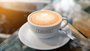 A white cup with latte art and the name 'CARLOS' on a saucer, placed on a wooden table.