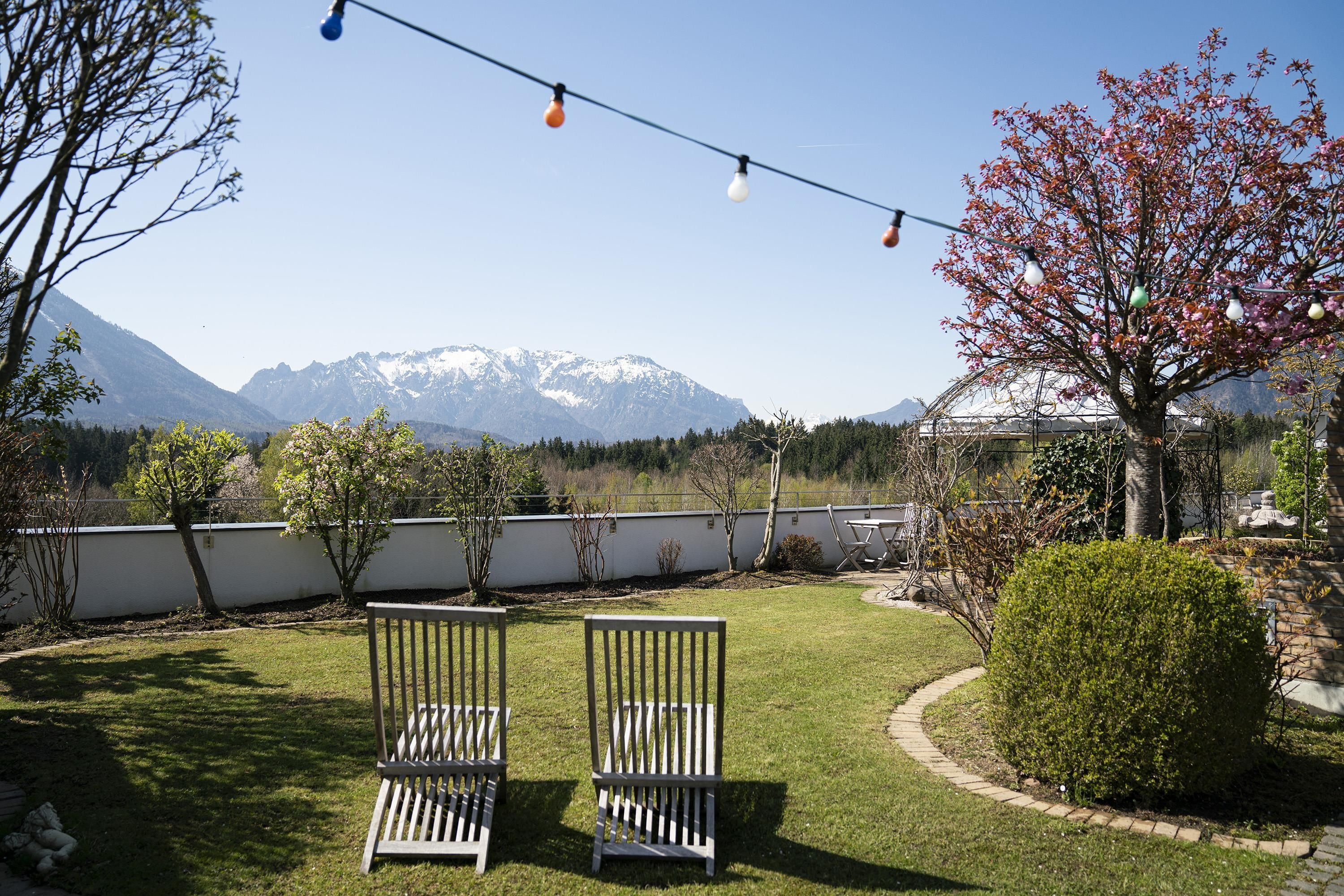 Un jardin avec deux chaises en bois, une guirlande lumineuse et une vue sur des montagnes enneigées.