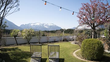 Un jardín con dos sillas de madera, luces colgantes y vistas a montañas nevadas.