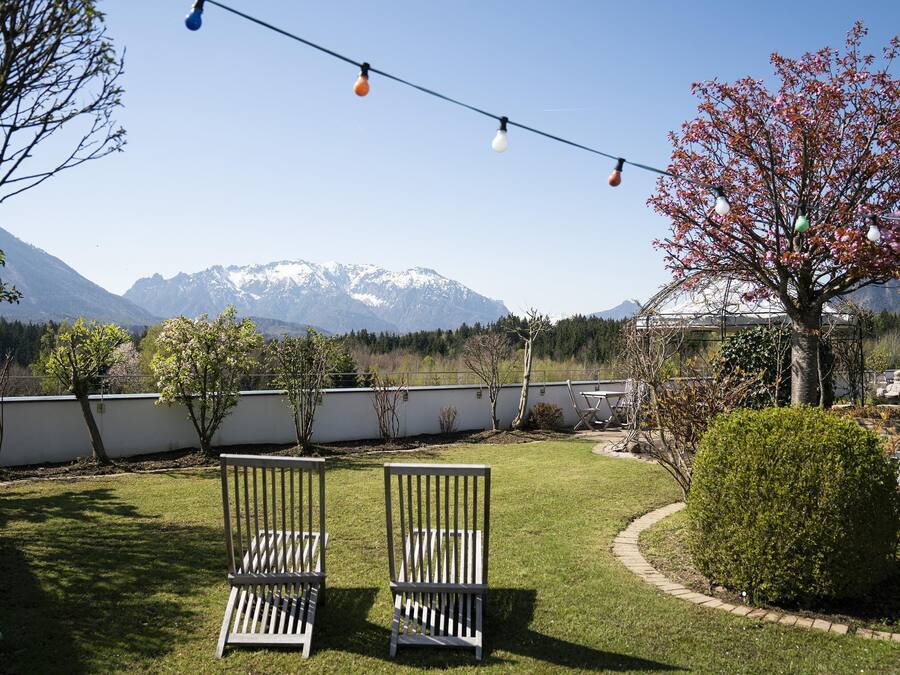 A garden with two wooden chairs, a string of lights, and a view of snow-capped mountains.
