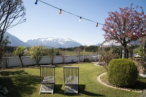 Un jardin avec deux chaises en bois, une guirlande lumineuse et une vue sur des montagnes enneigées.