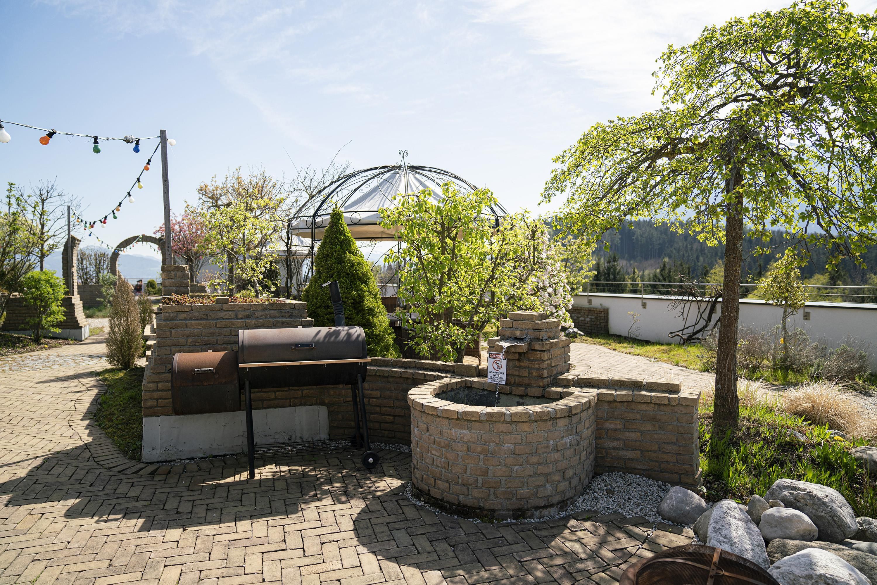 A patio area with a barbecue grill, a decorative brick planter, and a pergola structure.