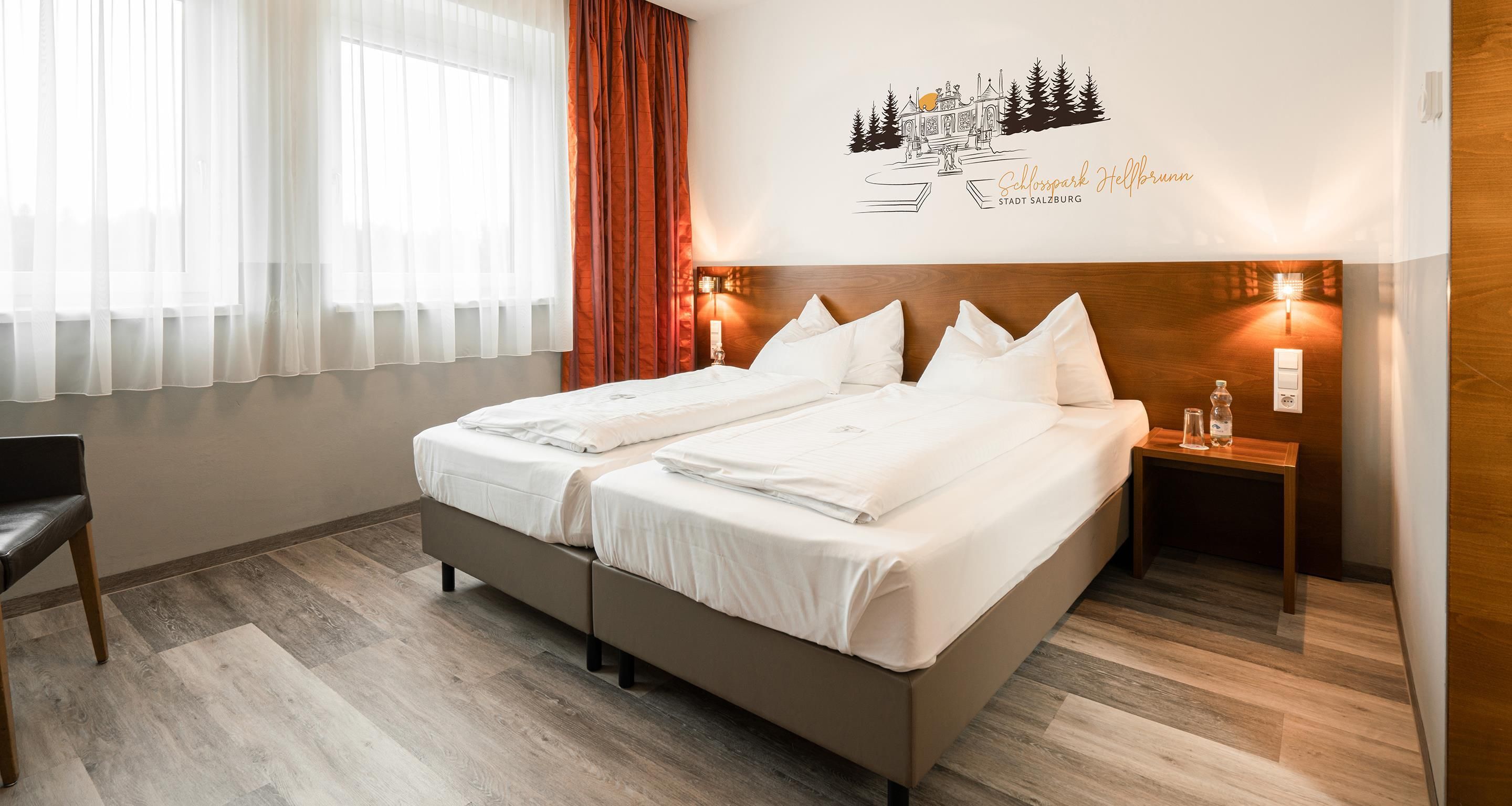 Habitación de hotel con cama doble, mesita de noche con lámpara, una silla y un adorno en la pared.
