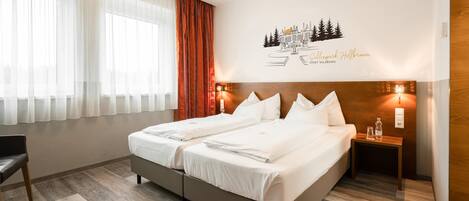 Habitación de hotel con cama doble, mesita de noche con lámpara, una silla y un adorno en la pared.