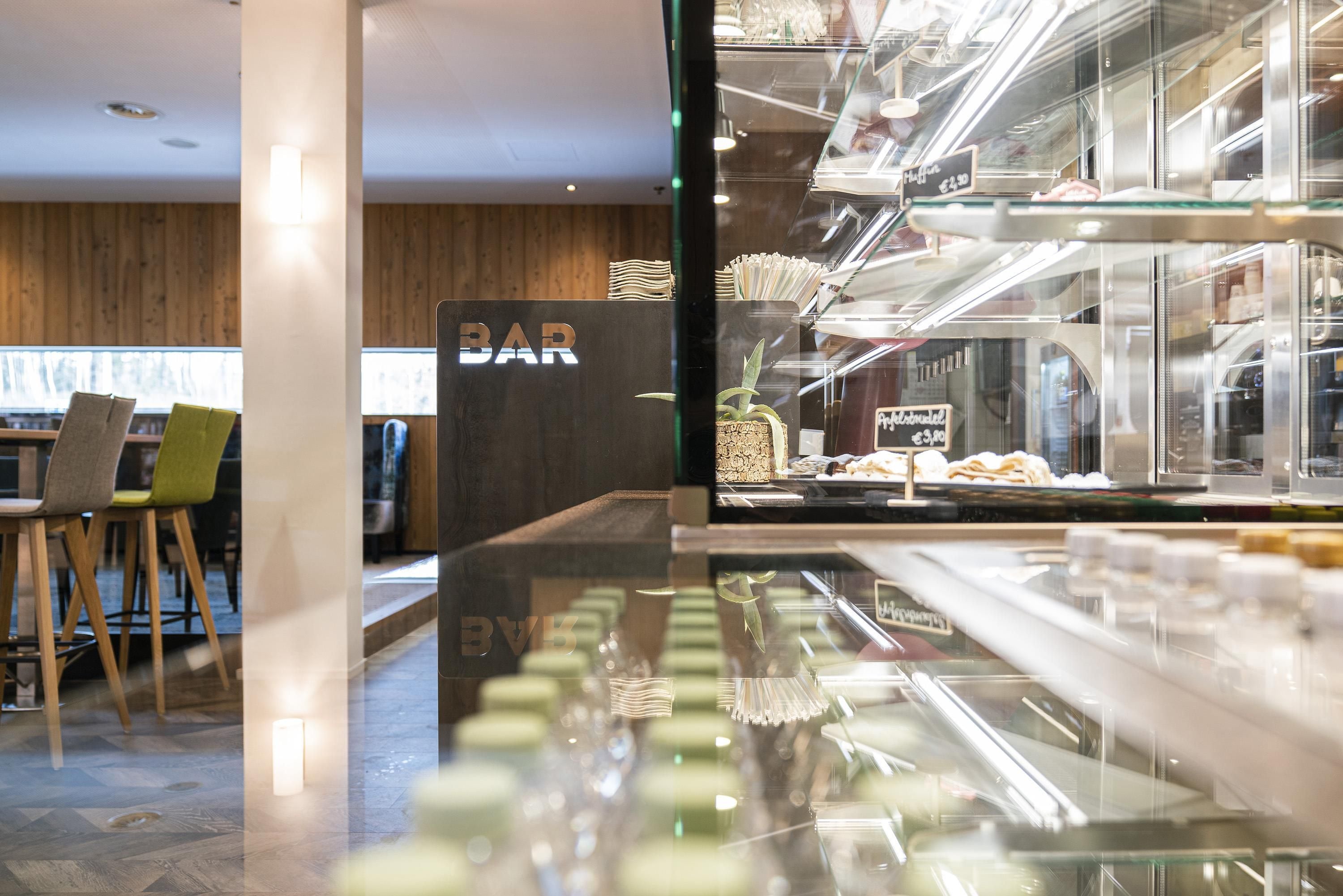 A modern interior with a bar area, wooden flooring, and a glass display case with food items.