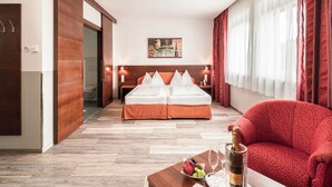 Habitación de hotel con cama doble, un sofá rojo, una mesa de centro de madera con una botella de champán y un cuadro en la pared.