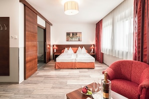 Habitación de hotel con cama doble, un sofá rojo, una mesa de centro de madera con una botella de champán y un cuadro en la pared.
