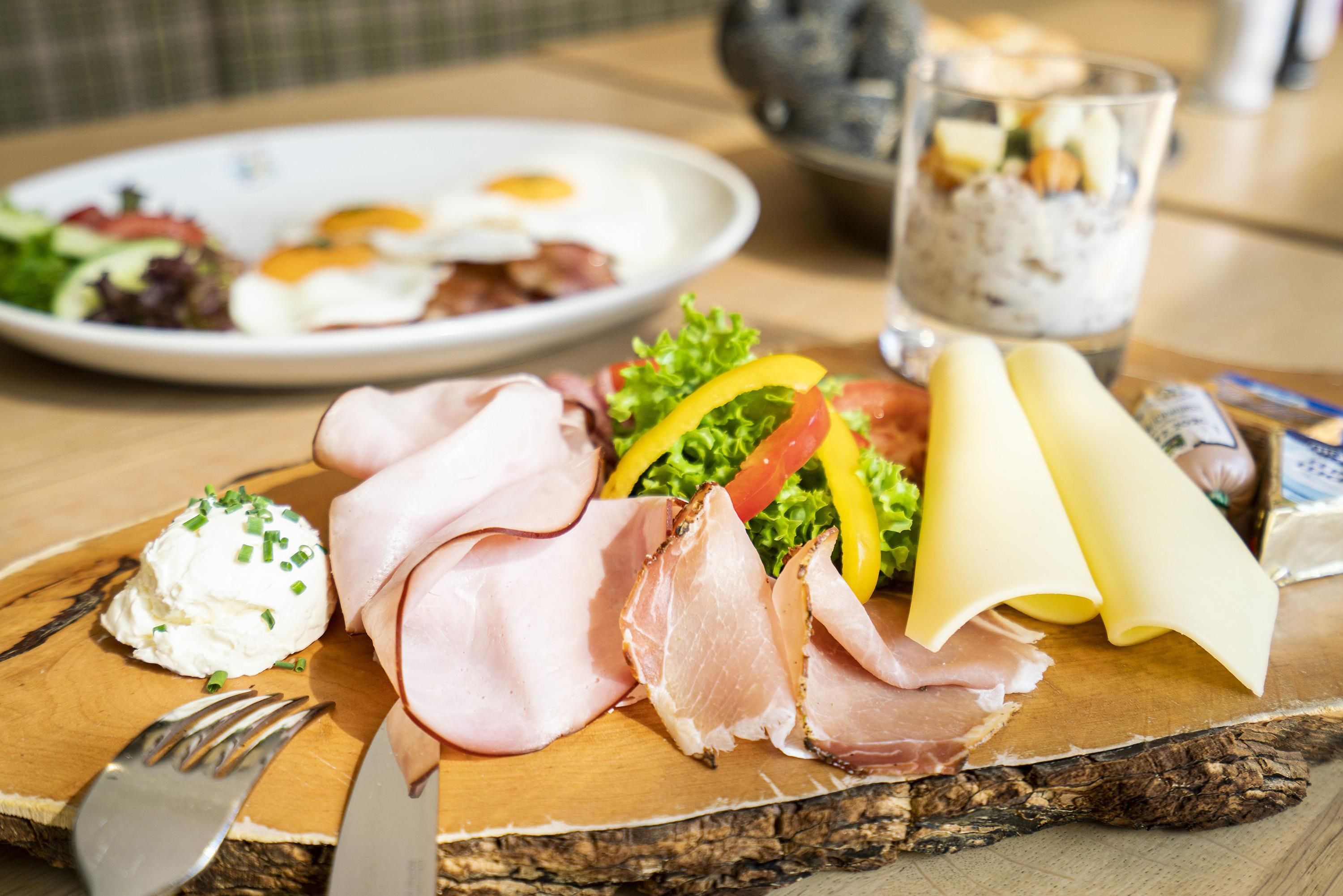 Una mesa de madera con diversas opciones de comida, incluyendo embutidos, una ensalada y un vaso de una bebida cremosa.