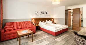 Une chambre d’hôtel avec un canapé rouge, une table en bois, un lit avec une literie blanche et une œuvre d’art accrochée au mur.