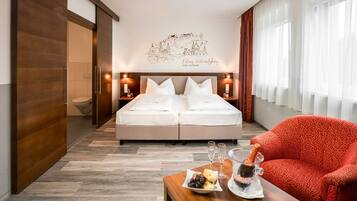 Ein Hotelzimmer mit Bett, einem roten Sessel, einem Frühstücksbrettchen und einem Stadtbild als Wandbild.