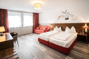 Ein Hotelzimmer mit einem Doppelbett, einem Schreibtisch mit Telefon, einem Sessel und einem roten Sofa, sowie einer Wanddekoration.