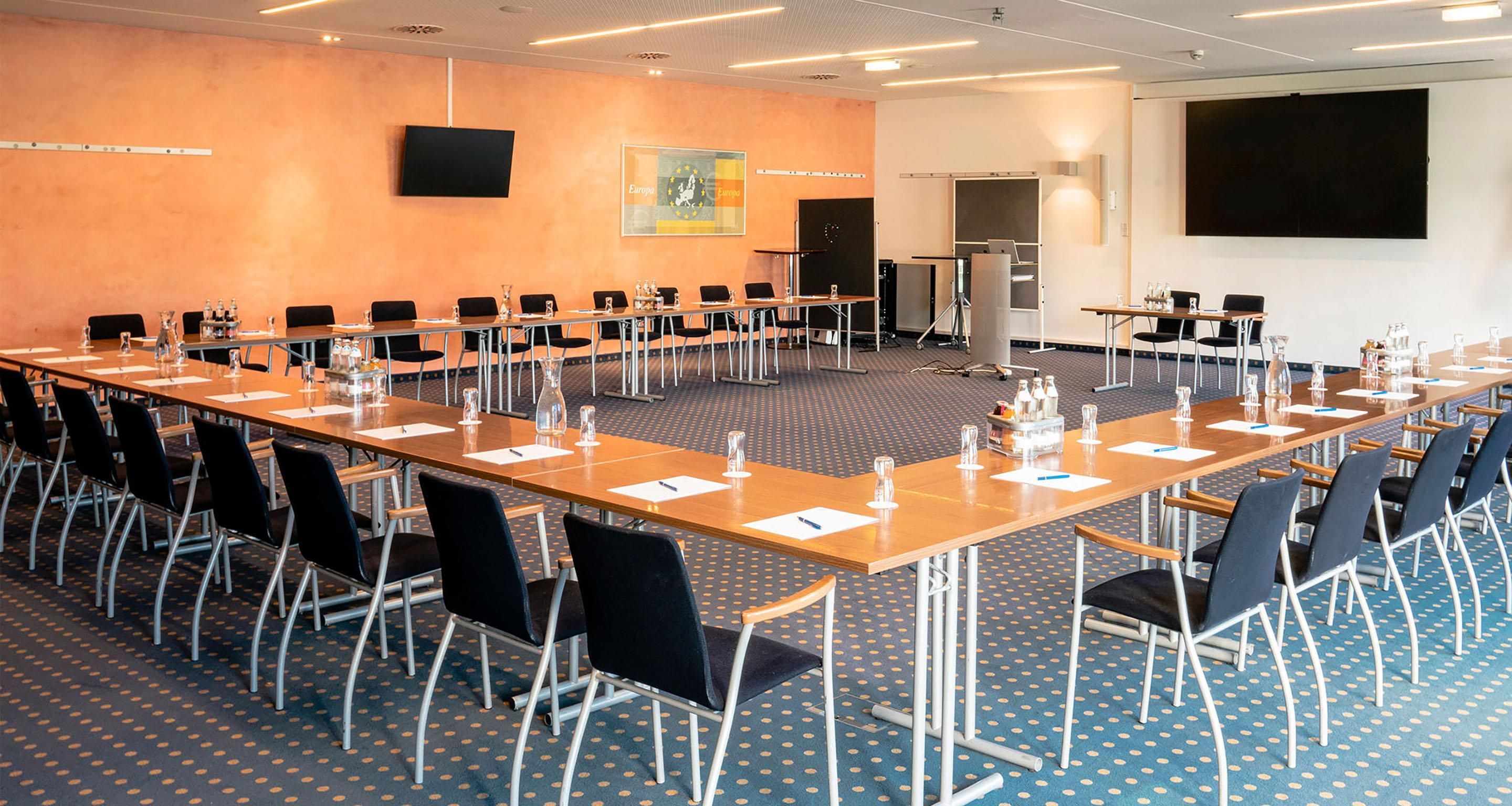 A conference room with a long table, chairs, and a projector screen.