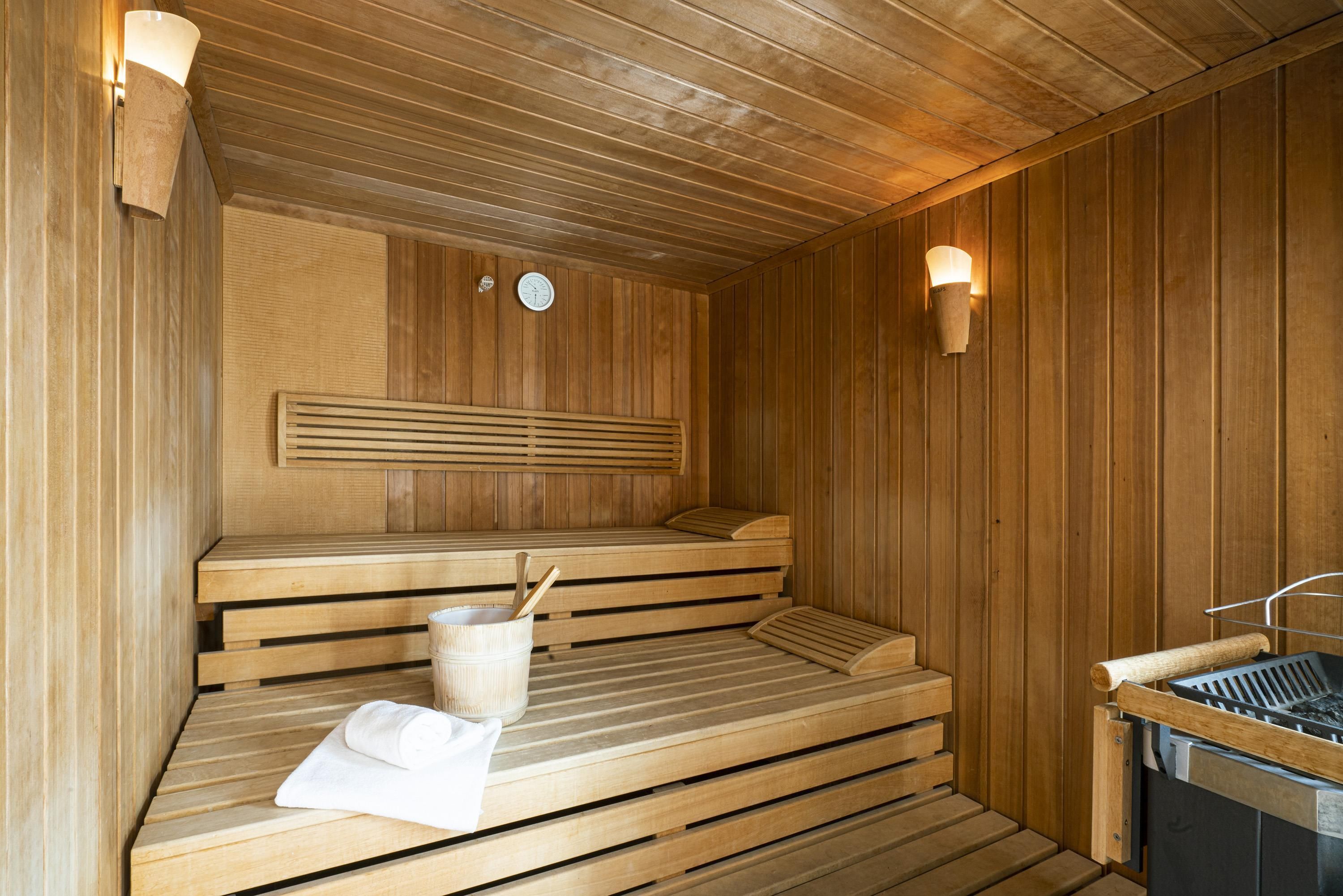 A sauna with wooden benches, a wall-mounted clock, and a towel on one bench.