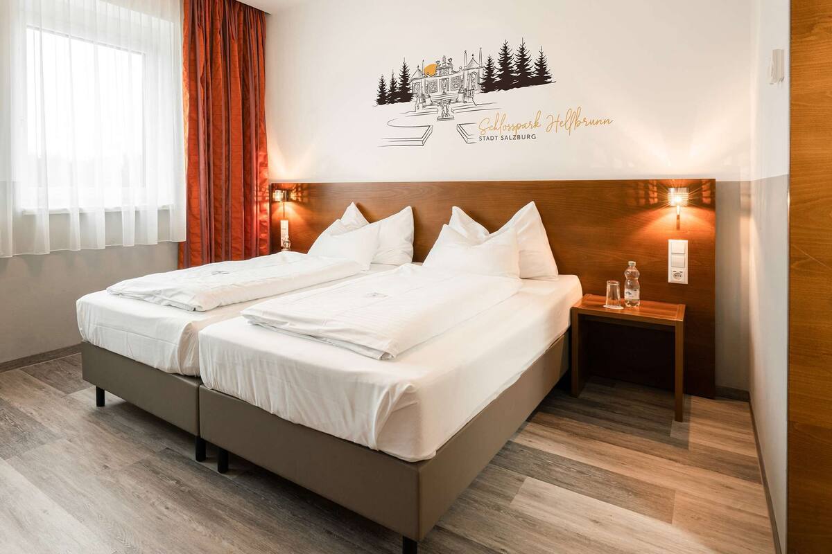 Una habitación de hotel con cama doble, una mesita de noche de madera, una silla y un adorno en la pared.