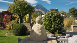 Una estàtua de Buda de pedra en un jardí amb muntanyes al fons i una arcada.