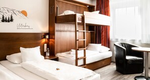 Een hotelkamer met een stapelbed, een bureau met stoel, een nachtkastje met lamp en een wandplank.
