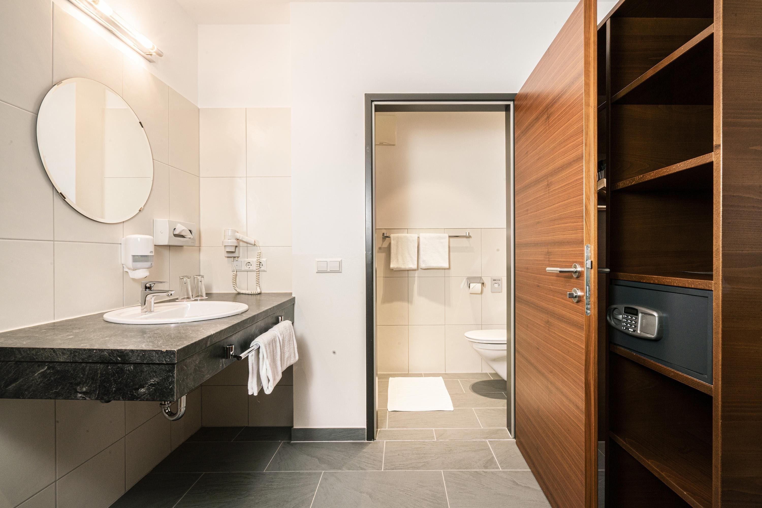 Une salle de bain moderne avec un comptoir en marbre, un miroir rond et un meuble-lavabo en bois.