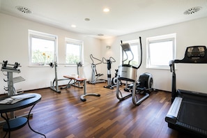 Un gimnasio con diversos equipos de ejercicio, amplias ventanas y suelo de madera.