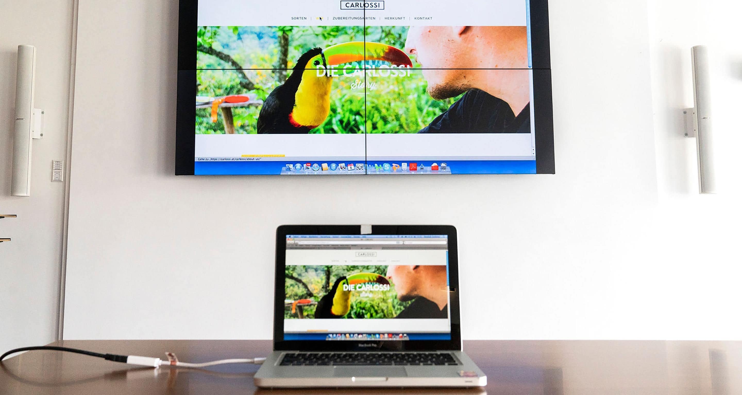 A laptop displaying a website with a toucan and a man, connected to a monitor above it.