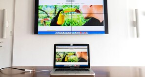 A laptop displaying a website with a toucan and a man, connected to a monitor above it. - Best Western Hotel am Walserberg (Wals-Siezenheim)