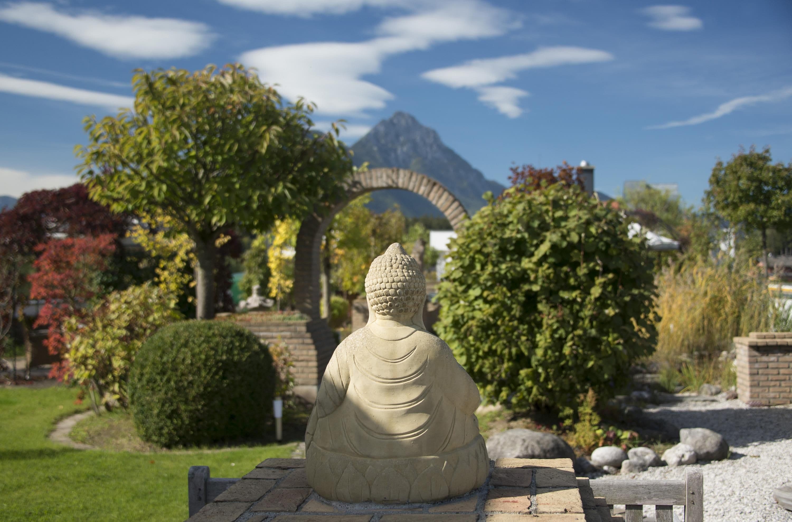 Une statue de Bouddha en pierre, dans un jardin, avec une montagne en arrière-plan.