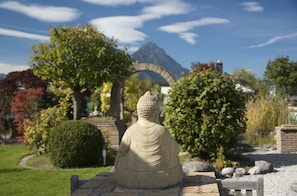 Een stenen Boeddhabeeld in een tuin, met een berg op de achtergrond.