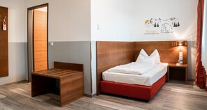Une chambre d’hôtel avec un lit, un banc en bois, une table de chevet et un luminaire fixé au mur.