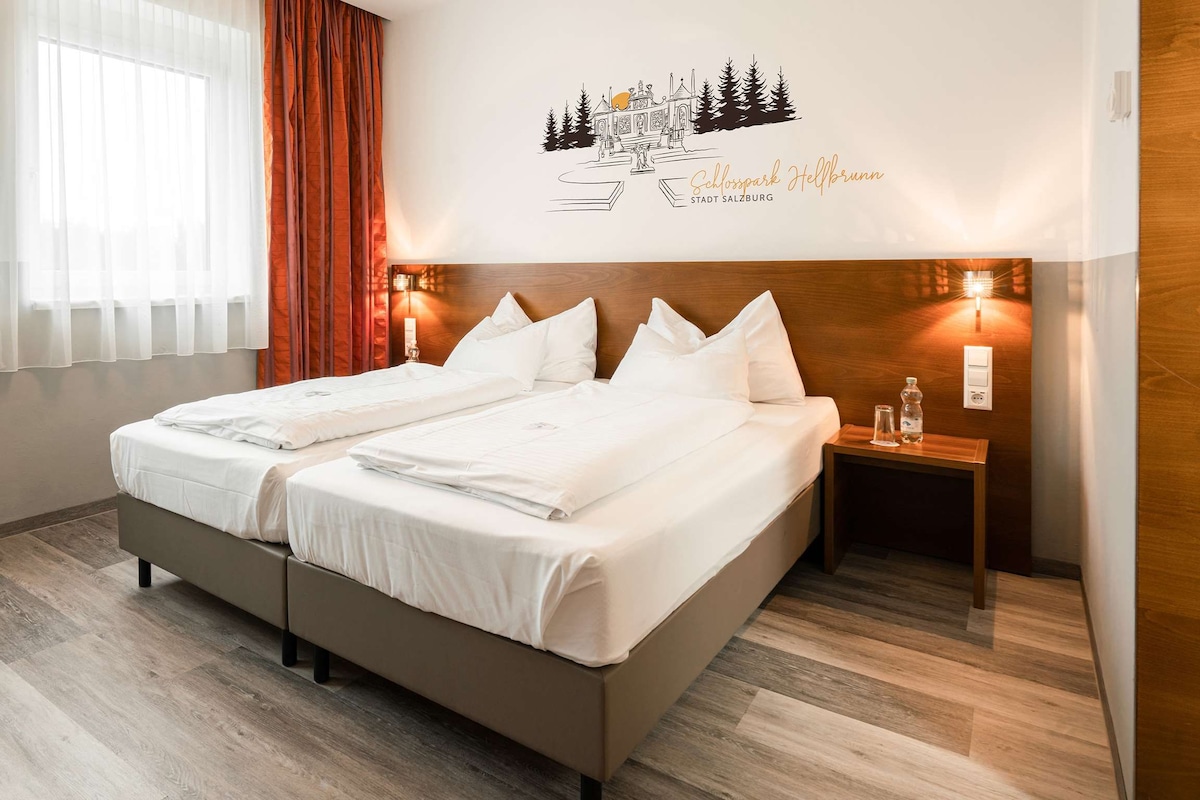 Une chambre d’hôtel avec un lit double, une table de chevet en bois, une chaise et un élément décoratif mural.