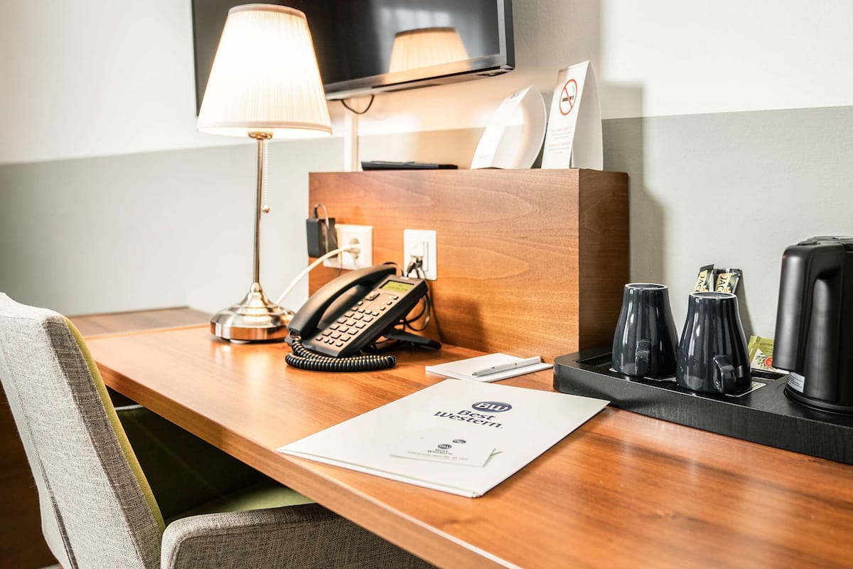 Escritorio de habitación de hotel con teléfono, lámpara, cafetera y menú.