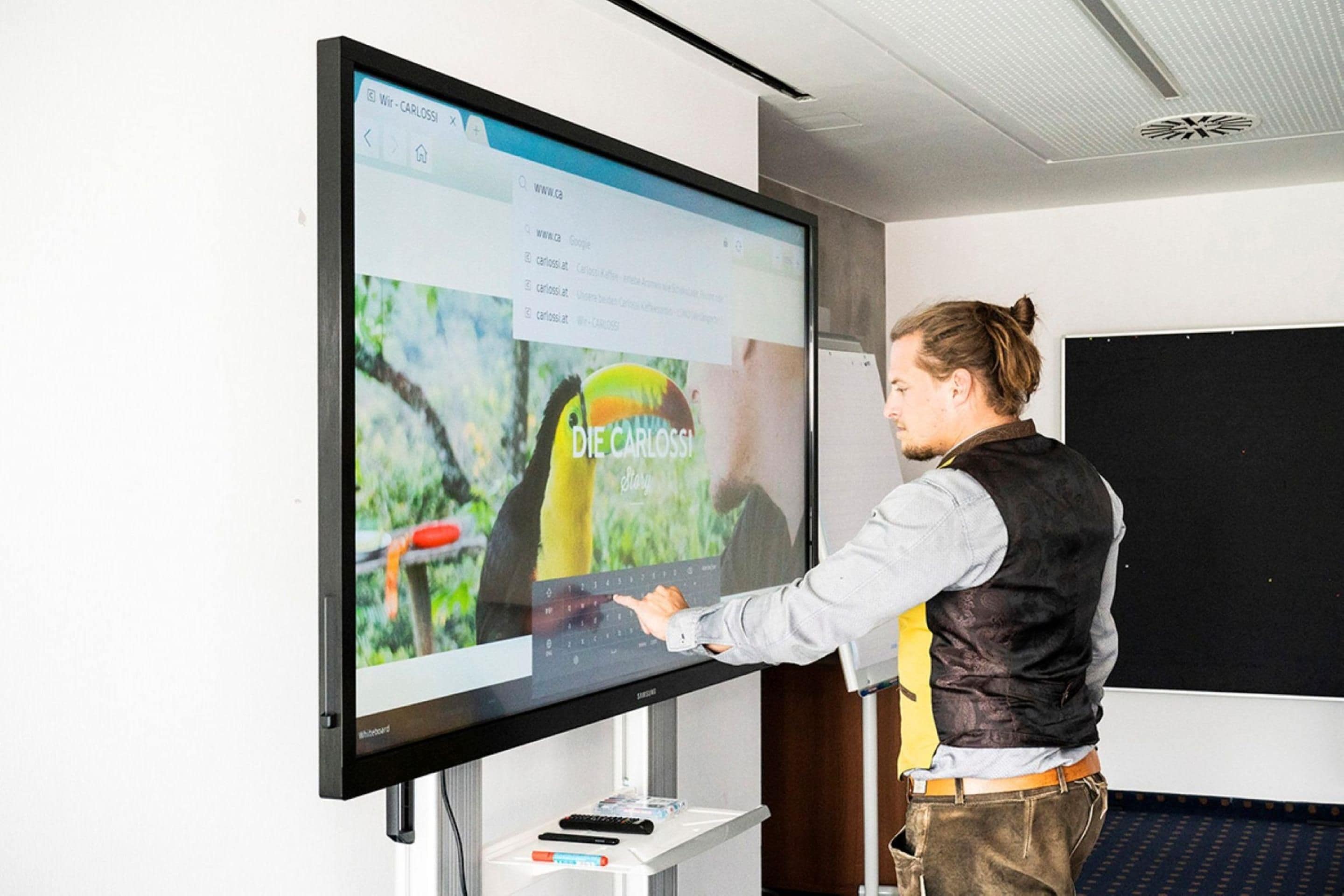 Eine Person präsentiert vor einer großen Leinwand, auf der eine Webseite angezeigt wird.