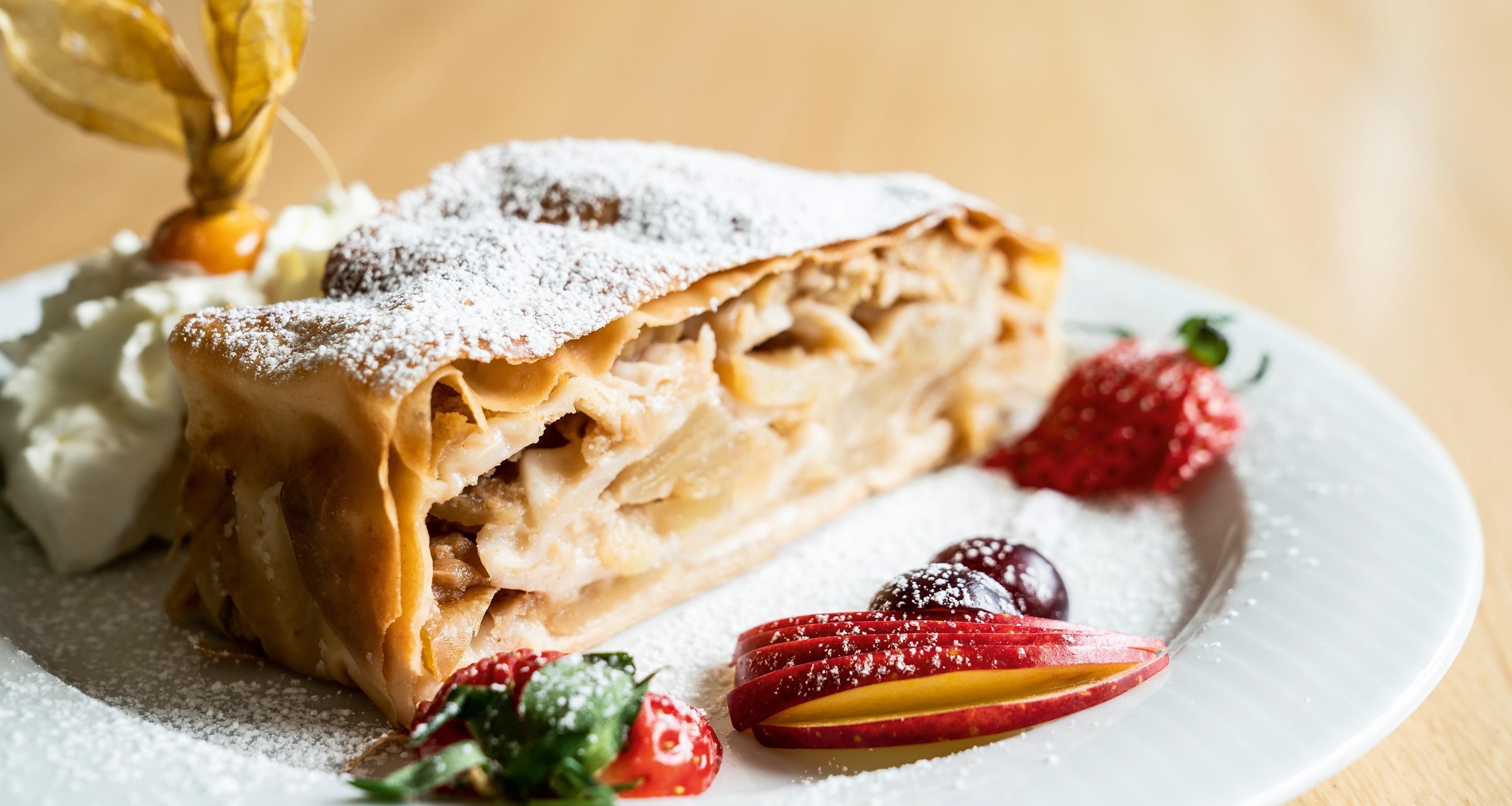 Un plato de postre con un pastel enrollado, crema batida y frutas en rodajas.