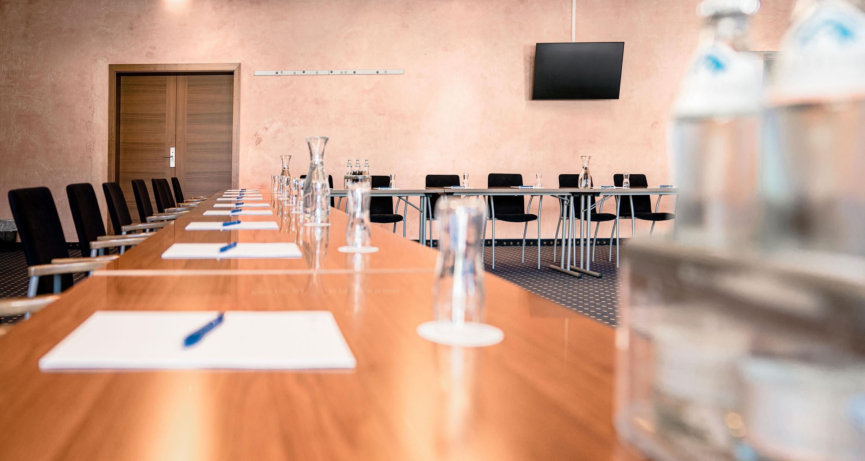 A conference room with a long table, chairs, and a television on the wall.