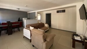 A living room with a sofa set, a dining area with a red table, and a kitchen in the background. - Residence Maeva (Mamoudzou)